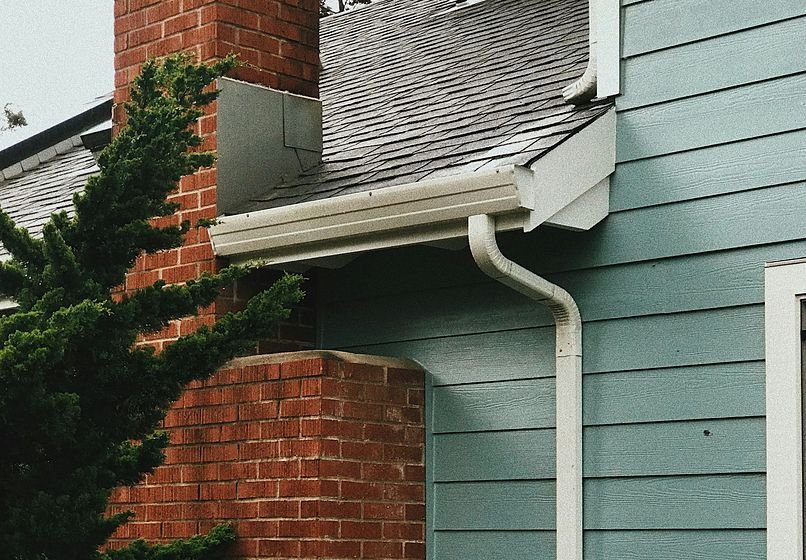 Gutter and downspout on a blue house with a brick chimney