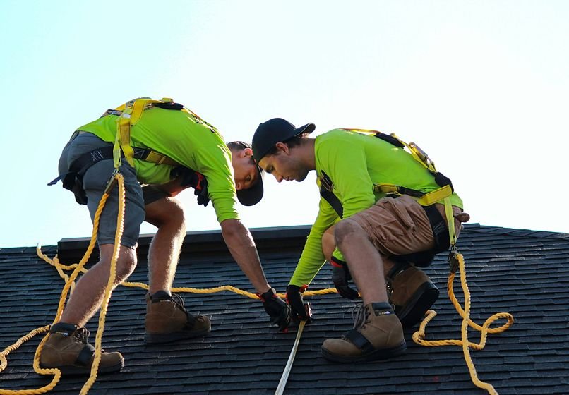 Two roofers measuring and laying shingles on a roof